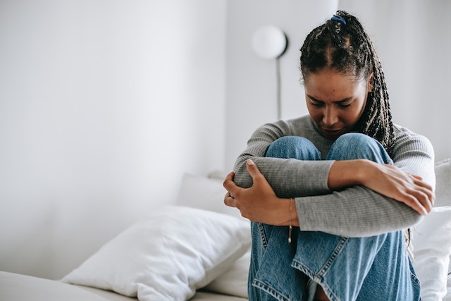 woman sitting on bed hugging knees