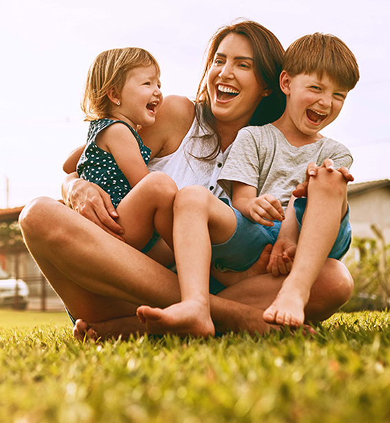 mother and her son and daughter laughing together sitting outside on grass